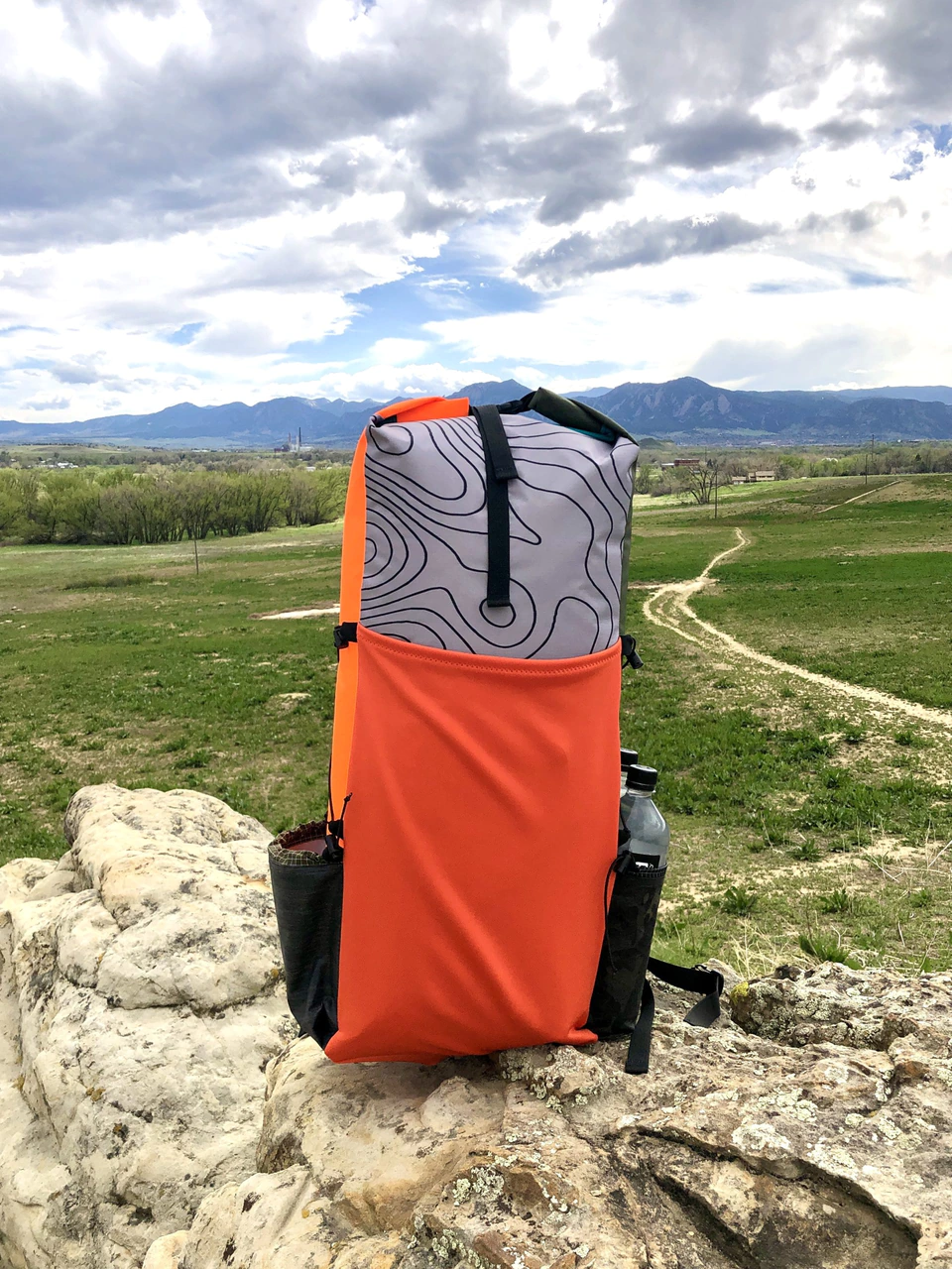 Finished DIY 30L ultralight backpack in orange and gray topo fabric on a rock with mountains behind